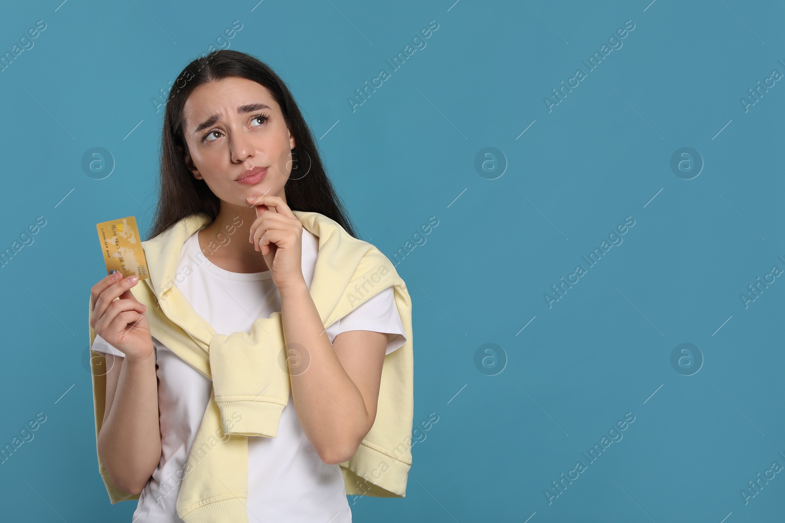 Photo of Curious woman with credit card on light blue background, space for text. Debt problem