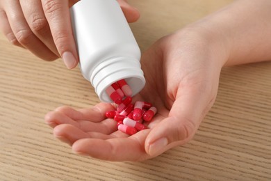 Photo of Woman pouring pills from bottle at wooden table, closeup