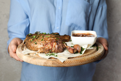 Photo of Woman holding wooden board with delicious grilled steak on grey background, closeup