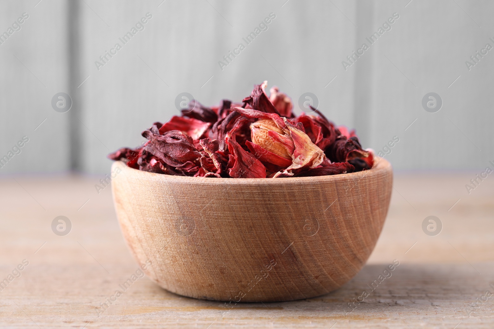 Photo of Dry hibiscus tea in bowl on wooden table, closeup