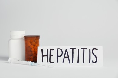Word Hepatitis and bottles of pills on white background