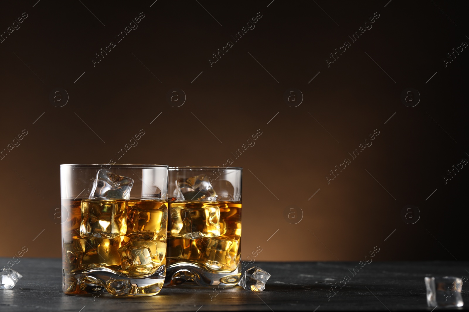 Photo of Whiskey and ice cubes in glasses on black table, closeup. Space for text