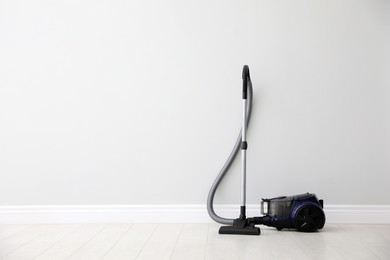 Photo of Modern vacuum cleaner near light wall indoors, space for text