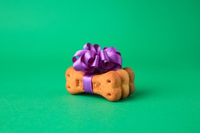 Photo of Bone shaped dog cookies with purple bow on green background