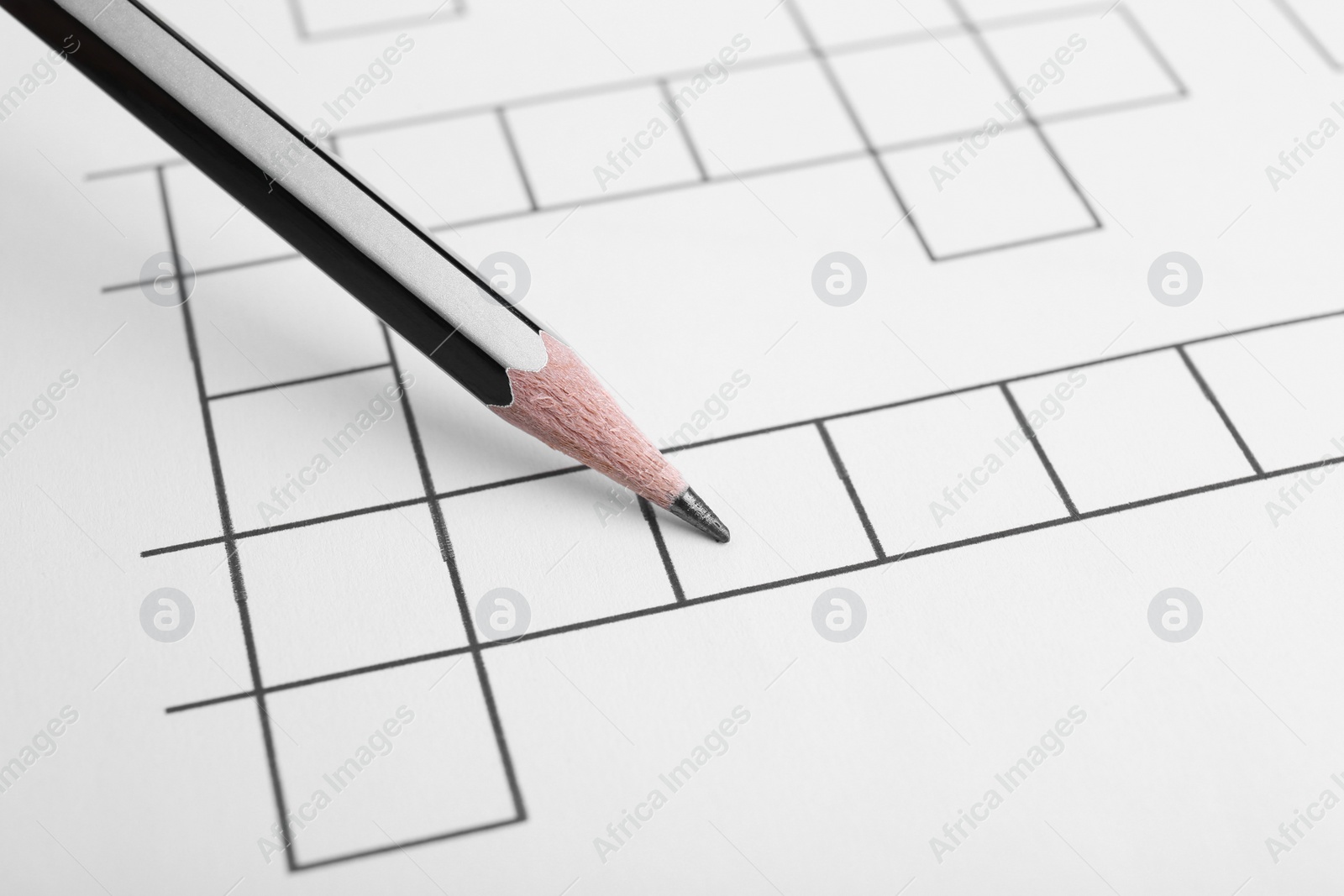 Photo of Pencil on blank crossword, closeup view. Intellectual entertainment