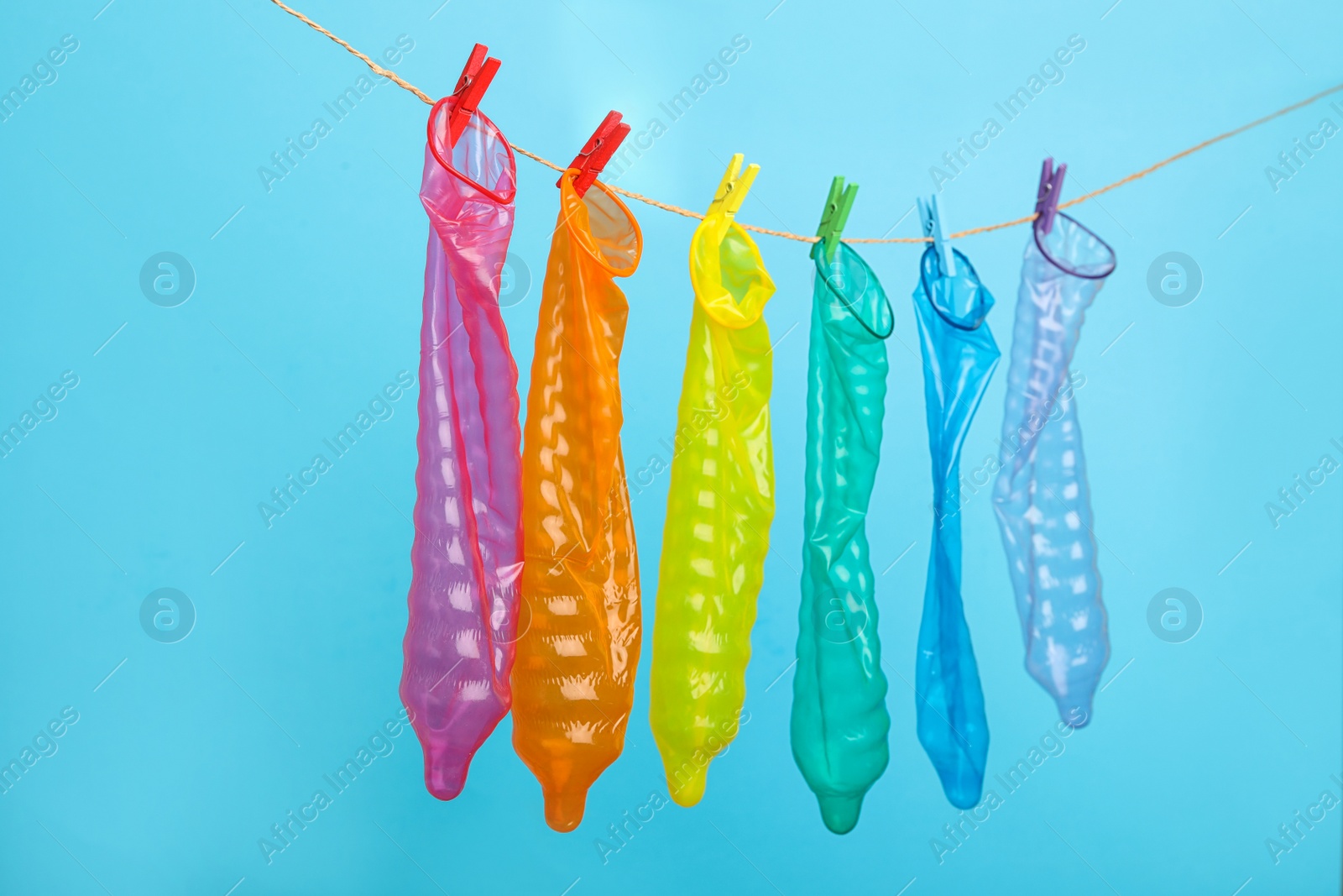 Photo of Used colorful condoms hanging on clothesline against light blue background. Safe sex concept