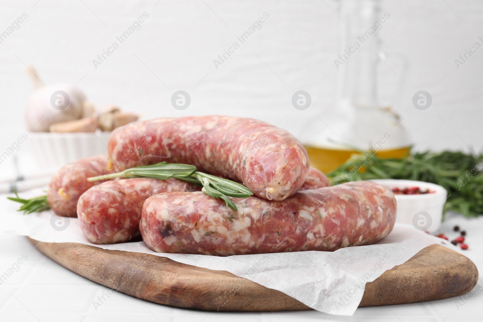 Photo of Raw homemade sausages and rosemary on white table, closeup