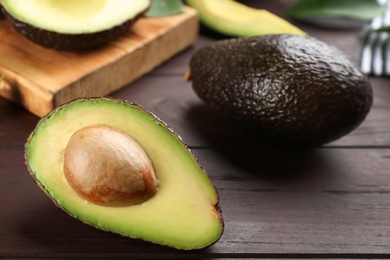 Photo of Whole and cut avocados on wooden table, closeup