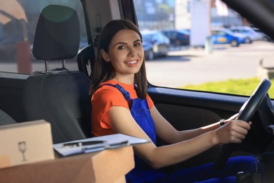 Photo of Courier with clipboard and parcels in car. Delivery service