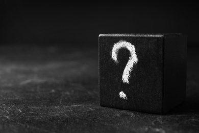 Photo of Wooden cube with question mark on black stone table, closeup. Space for text