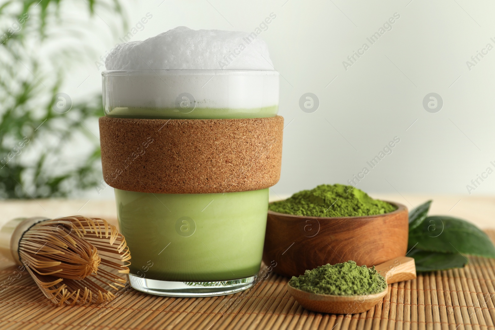 Photo of Glass cup of fresh matcha latte, powder and bamboo whisk on table, closeup