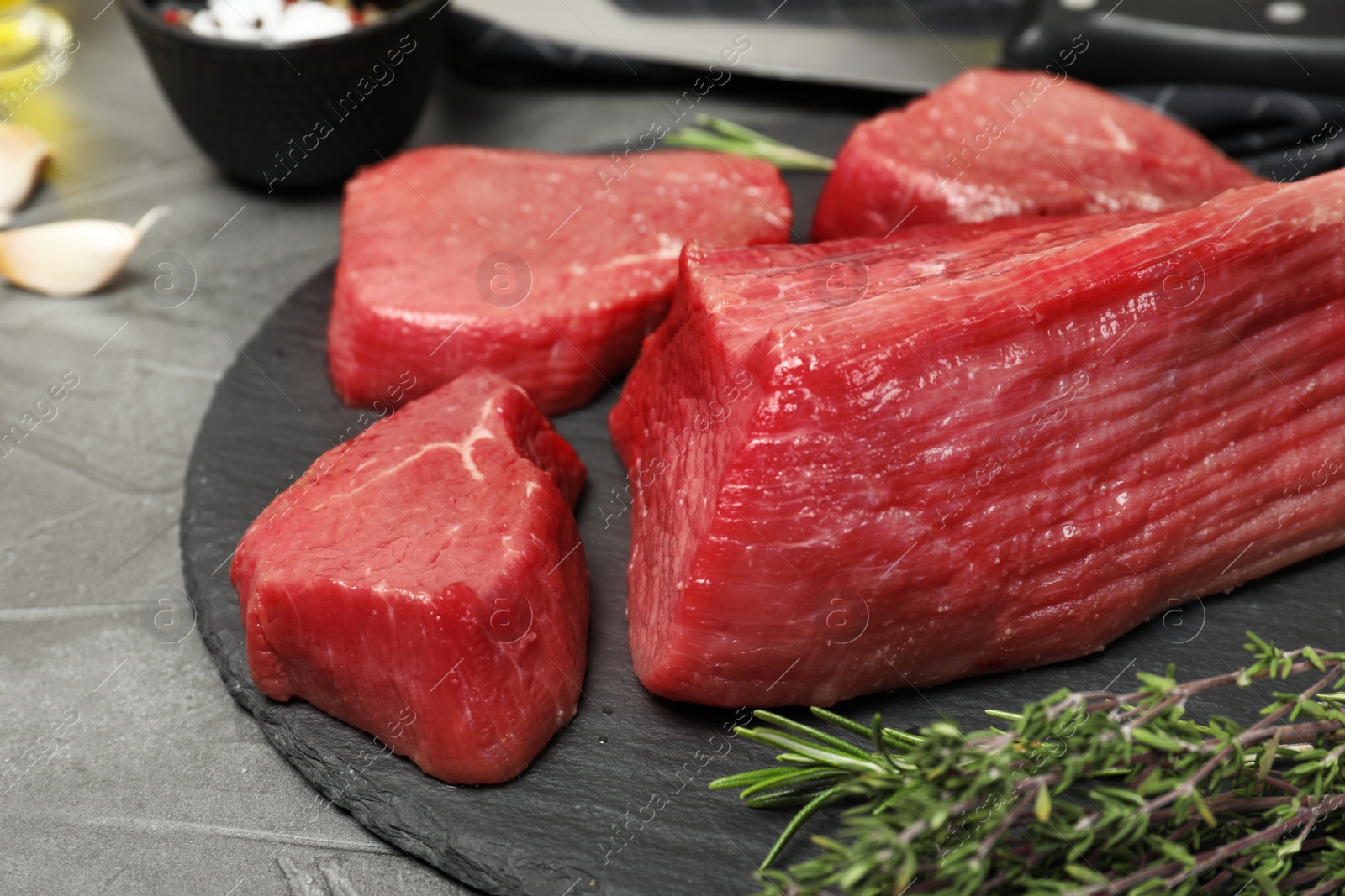 Photo of Slate plate with fresh raw meat and herbs on gray table