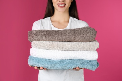 Photo of Young woman holding clean towels on color background, closeup. Laundry day