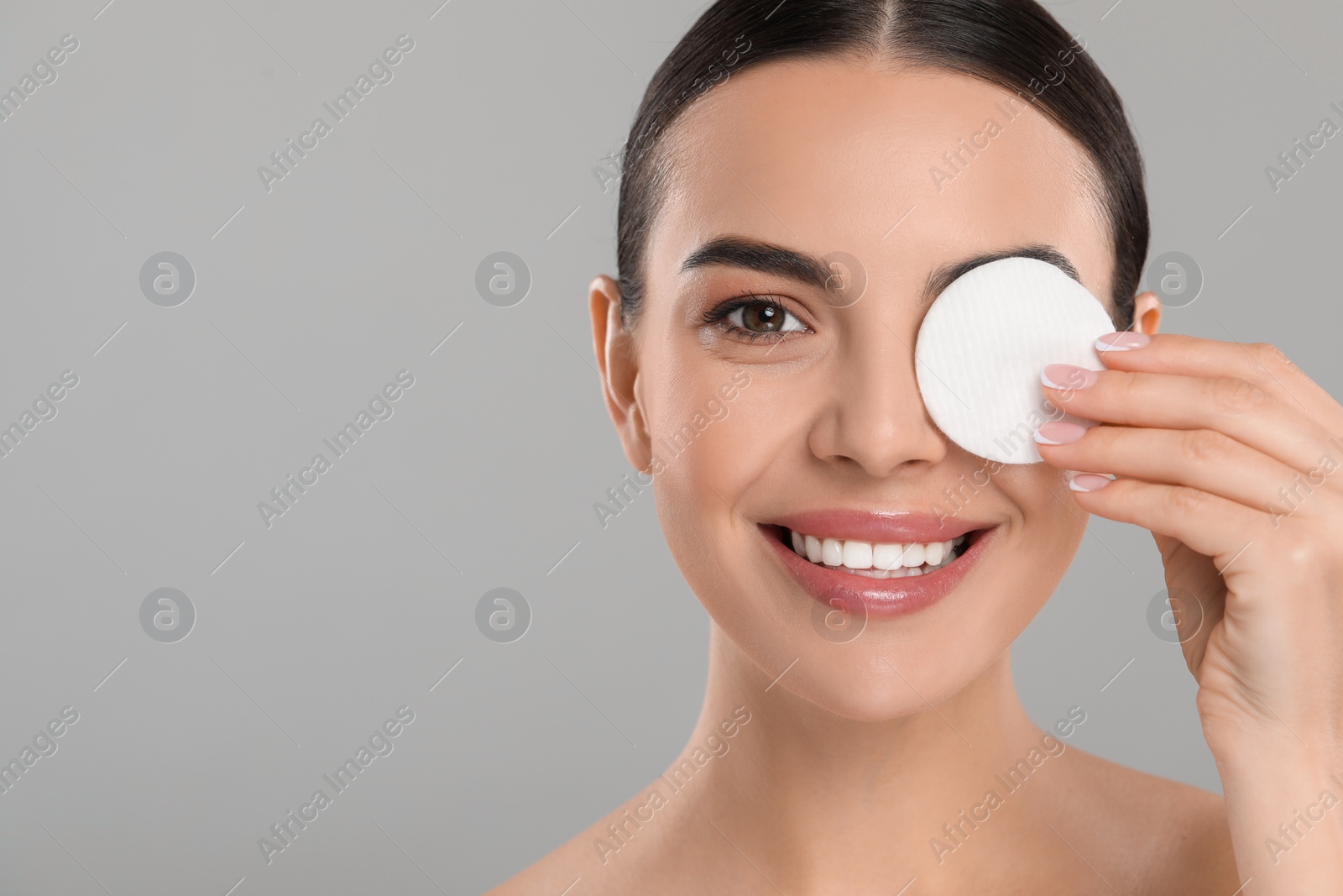Photo of Beautiful woman removing makeup with cotton pad on light grey background. Space for text