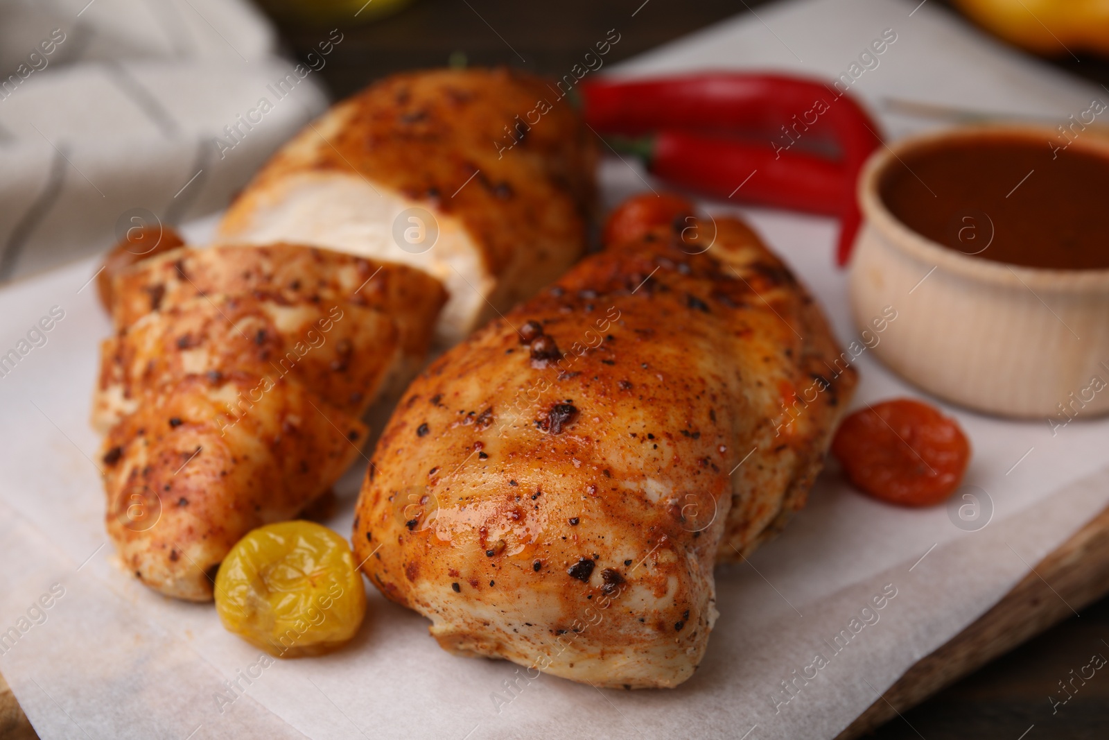 Photo of Baked chicken fillets and marinade on wooden table, closeup