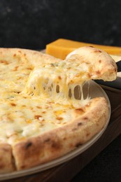 Photo of Taking piece of delicious cheese pizza at table, closeup