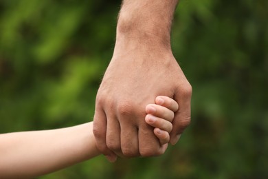 Photo of Man and child holding hands outdoors, closeup