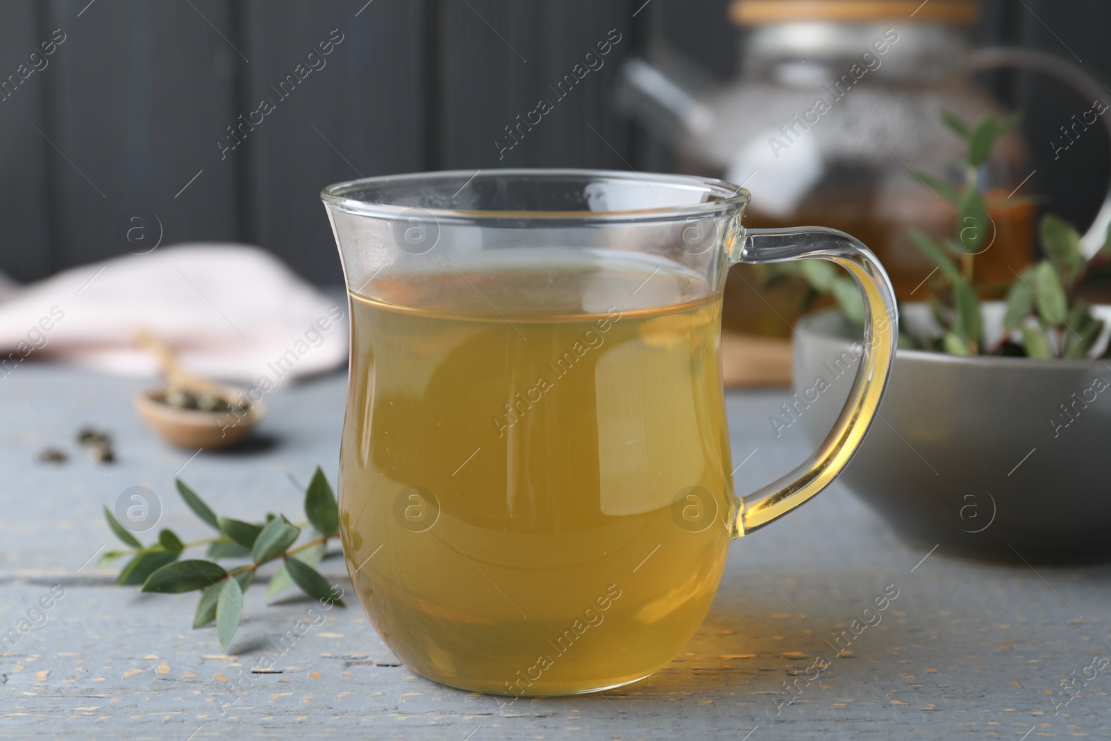 Photo of Glass cup of aromatic eucalyptus tea on grey wooden table, closeup