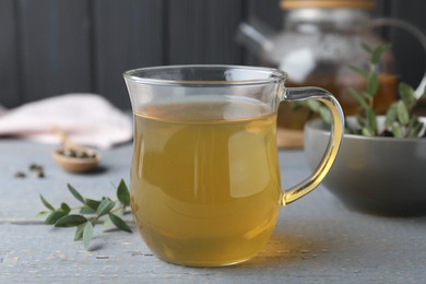 Glass cup of aromatic eucalyptus tea on grey wooden table, closeup