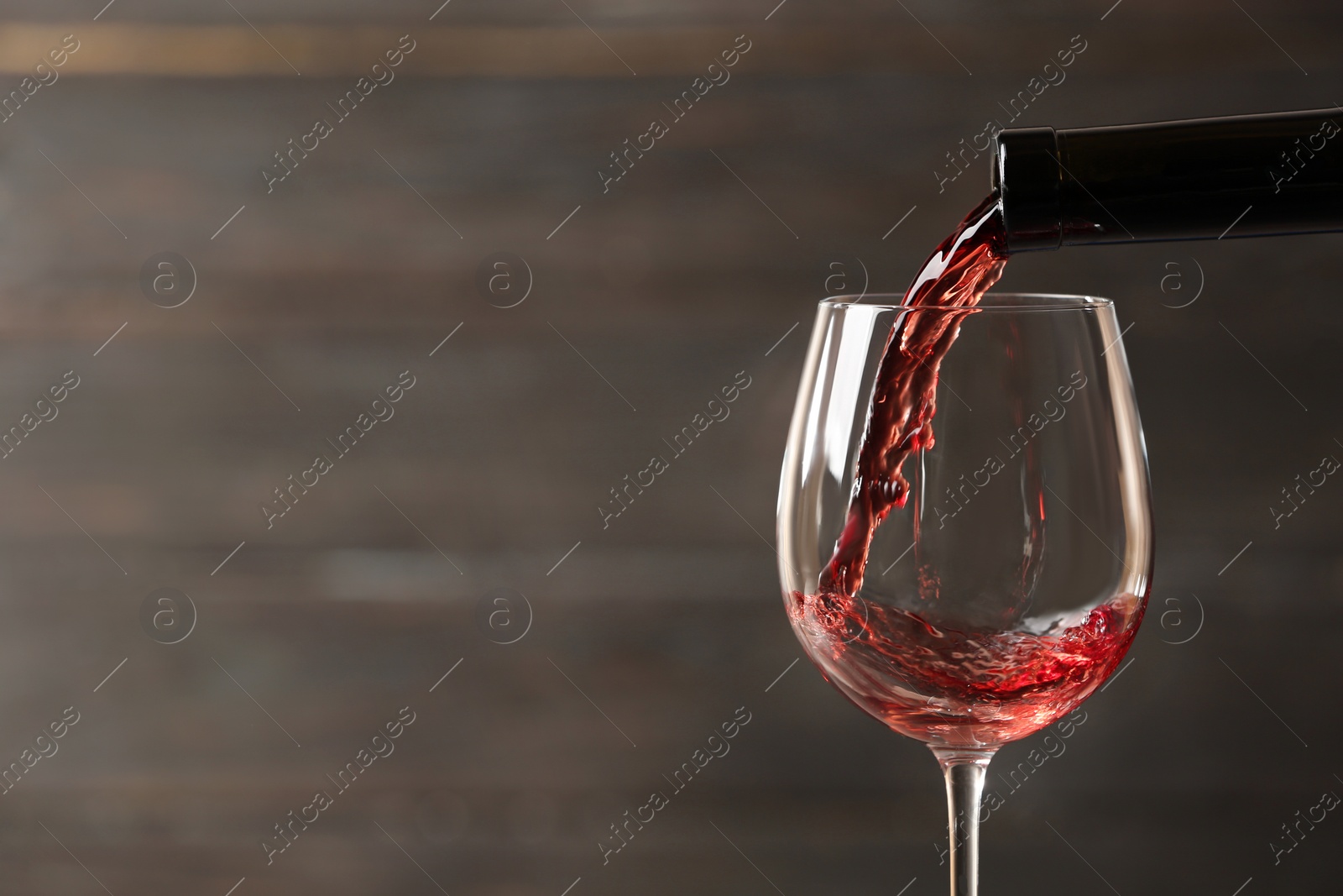 Photo of Pouring red wine into glass from bottle against blurred wooden background, closeup. Space for text