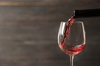 Pouring red wine into glass from bottle against blurred wooden background, closeup. Space for text