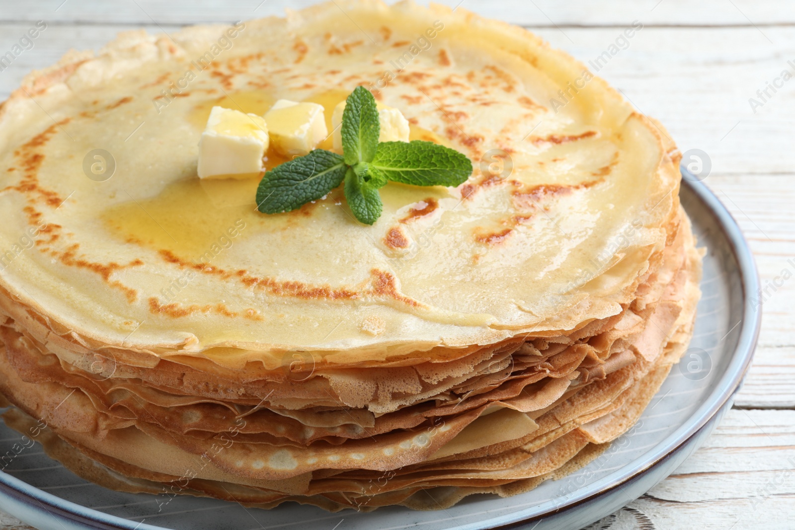 Photo of Stack of delicious crepes with mint and melting butter on white wooden table, closeup