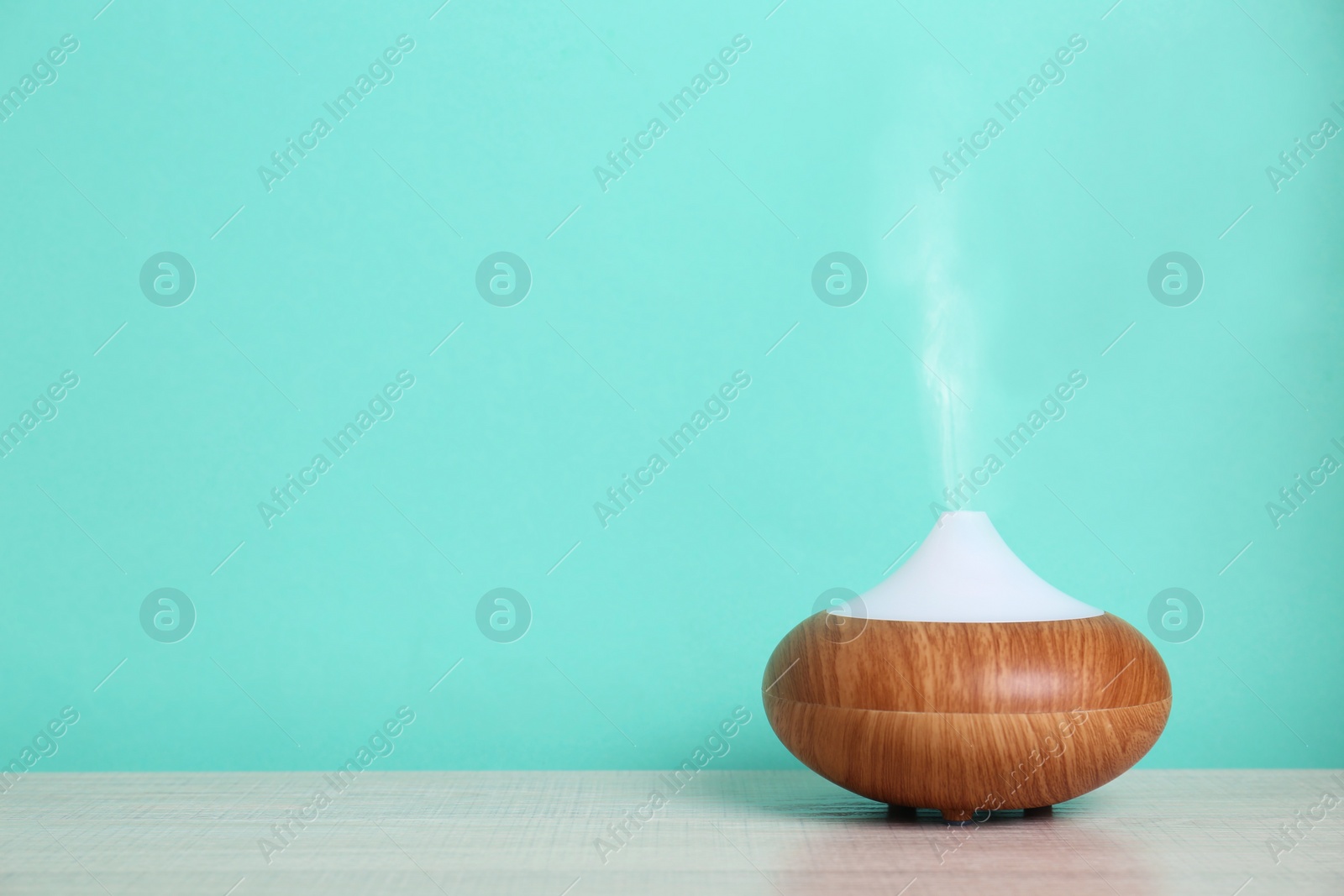 Photo of Essential oils diffuser on table near turquoise wall. Space for text