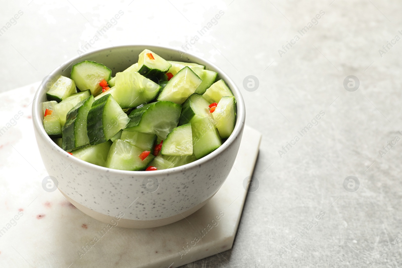 Photo of Delicious cucumber salad in bowl with board on grey table. Space for text