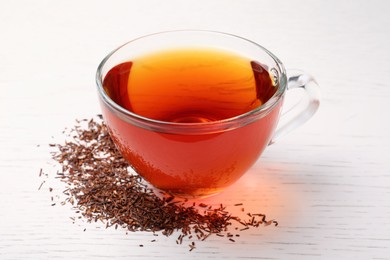 Photo of Freshly brewed rooibos tea and scattered dry leaves on white wooden table