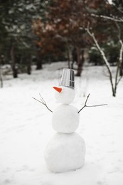 Cute snowman with metal bucket and carrot nose outdoors on winter day