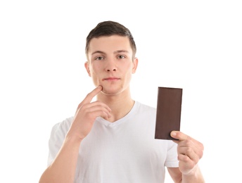 Young man with acne problem holding chocolate bar on white background. Skin allergy