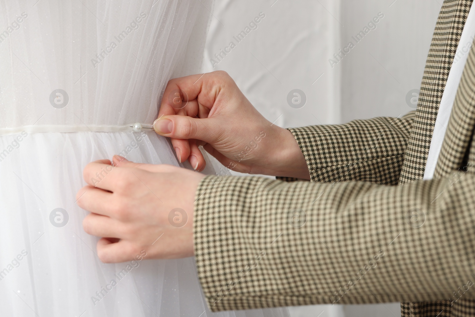 Photo of Dressmaker pinning pearl at mannequin with wedding dress in atelier, closeup