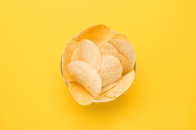 Photo of Bowl of tasty potato chips on yellow background, top view