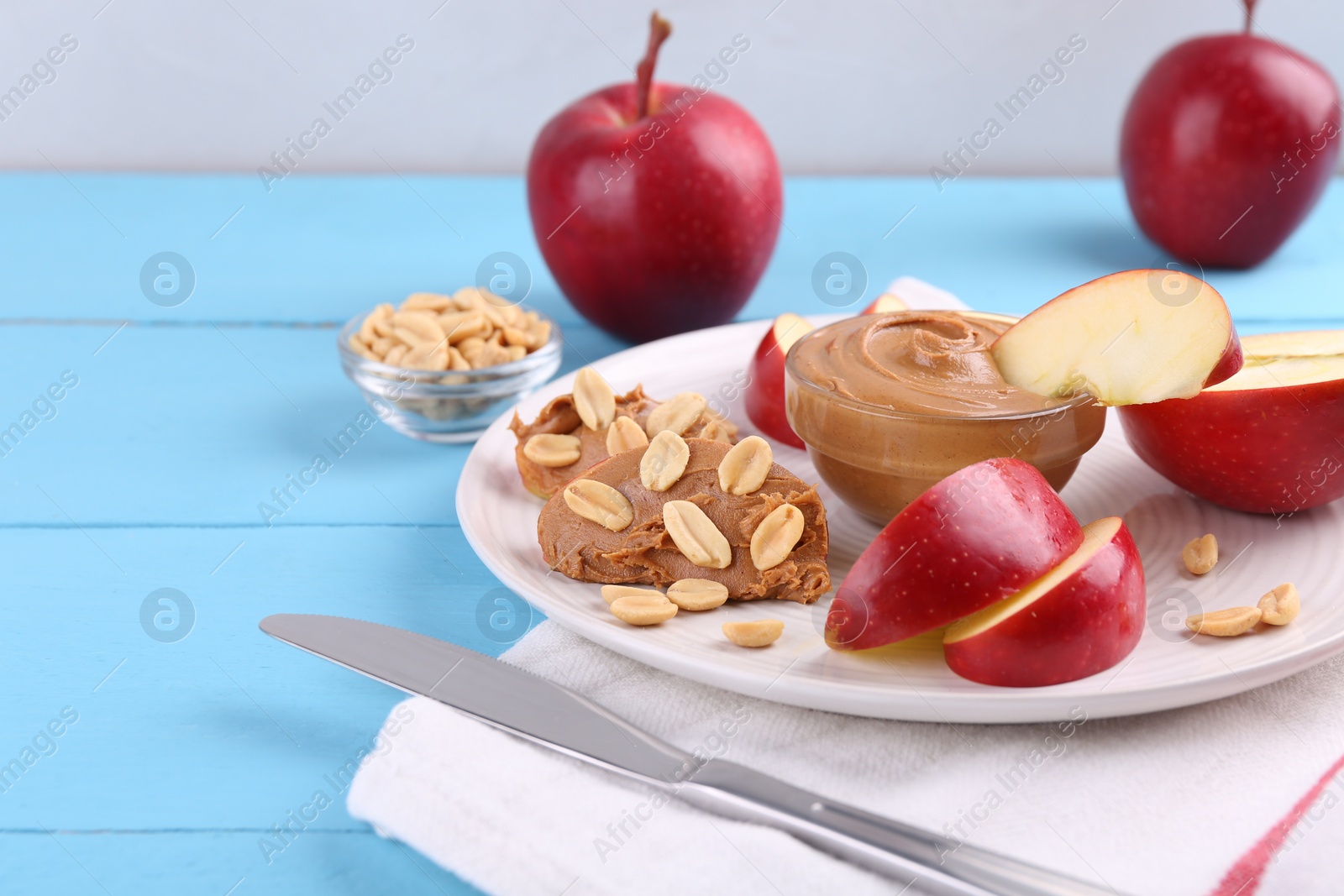 Photo of Slices of fresh apple with peanut butter, nuts and knife on light blue wooden table