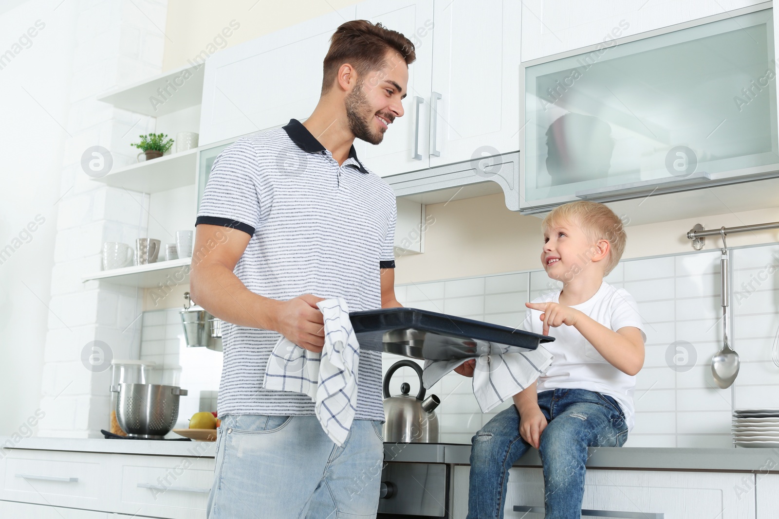 Photo of Young man and his son with oven sheet in kitchen