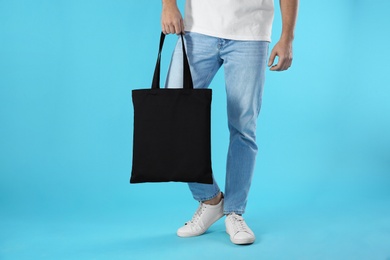 Young man holding textile bag on color background, closeup. Mockup for design