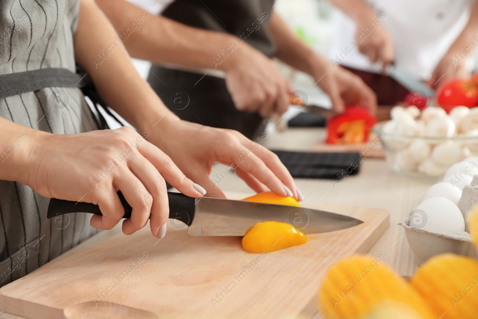 Photo of Female chef cutting paprika on wooden board at table, closeup