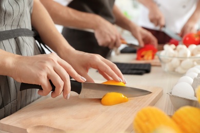 Photo of Female chef cutting paprika on wooden board at table, closeup