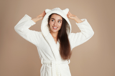 Photo of Beautiful young woman in bathrobe with funny hood on brown background