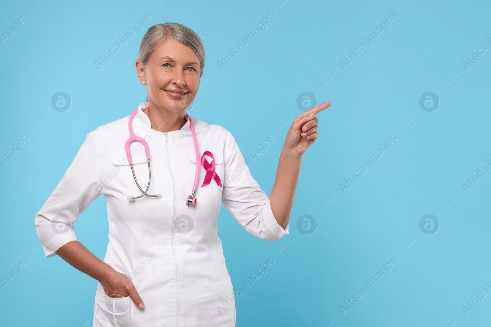 Photo of Doctor with pink ribbon and stethoscope on light blue background, space for text. Breast cancer awareness