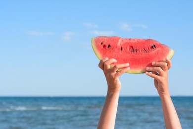 Photo of Child holding slice of fresh juicy watermelon near sea, closeup. Space for text