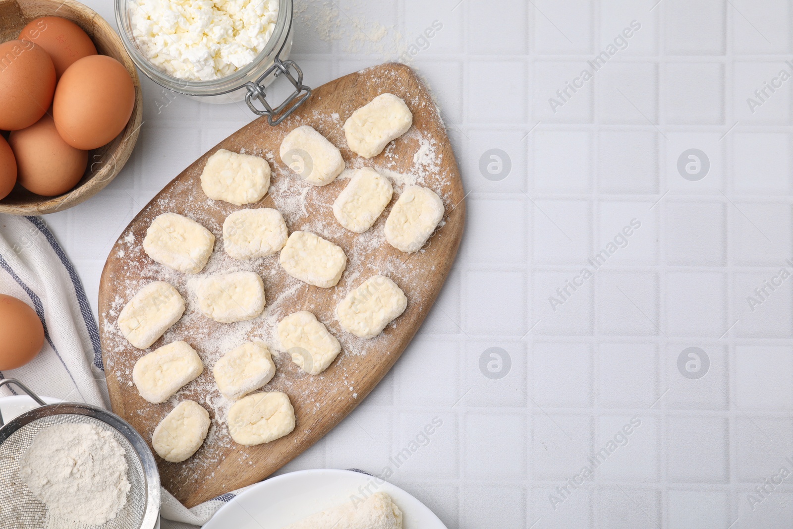 Photo of Making lazy dumplings. Board with cut dough and ingredients on white tiled table, flat lay. Space for text