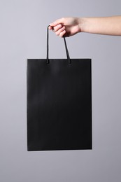 Woman holding paper shopping bag on grey background, closeup