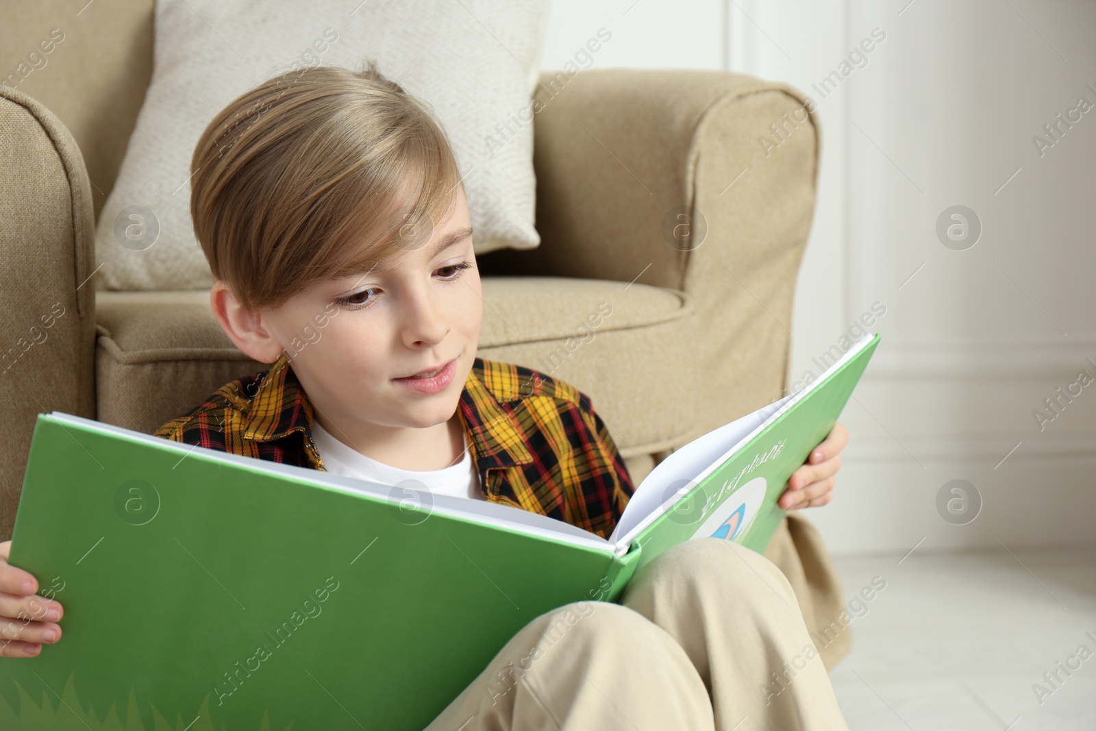 Photo of Little boy reading book on floor at home