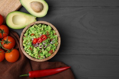 Photo of Bowl of delicious guacamole and ingredients on grey wooden table, flat lay. Space for text