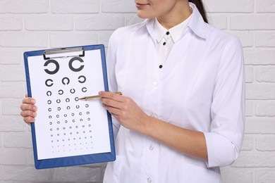 Ophthalmologist pointing at vision test chart near white brick wall, closeup