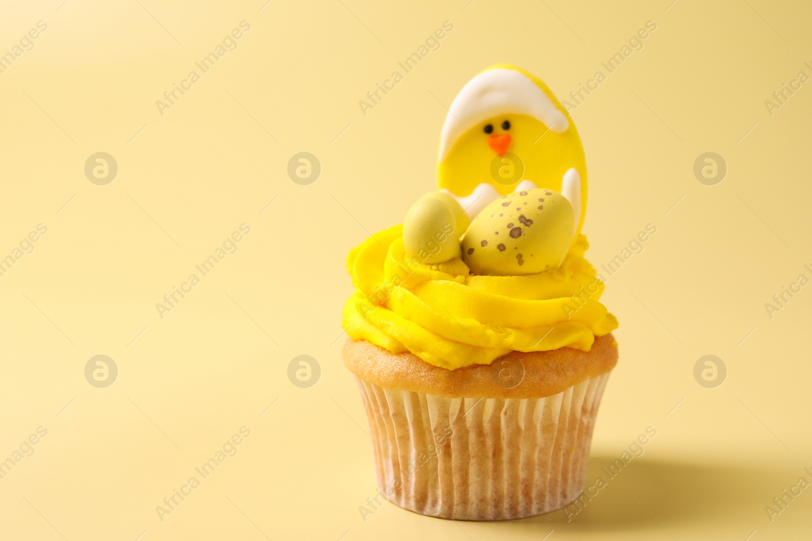 Photo of Tasty decorated Easter cupcake on pale yellow background, closeup. Space for text