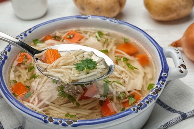Photo of Spoon with fresh homemade chicken soup over dish, closeup