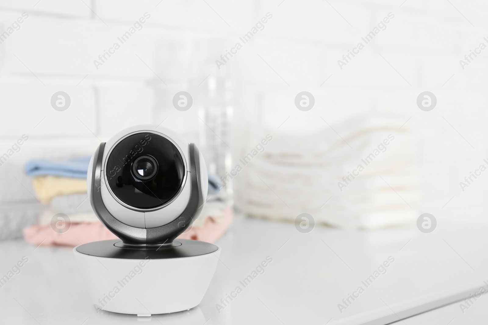 Photo of Baby camera on table near white brick wall, space for text. Video nanny