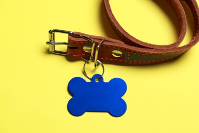 Leather dog collar with blue tag in shape of bone on yellow background. Space for text